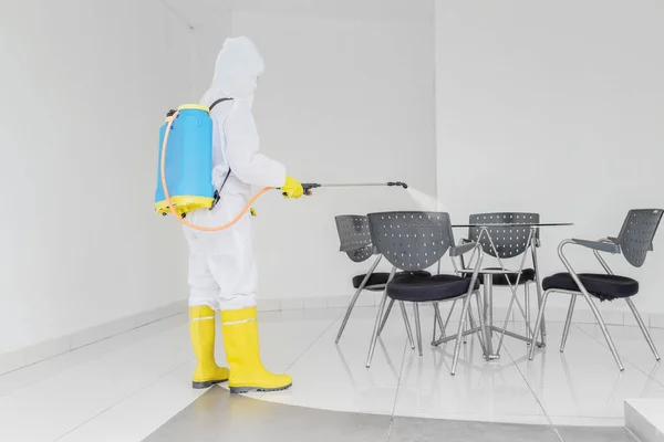 コロナウイルスのパンデミックの間 テーブルと椅子に消毒剤を噴霧しながら保護服を着ている若い男 — ストック写真