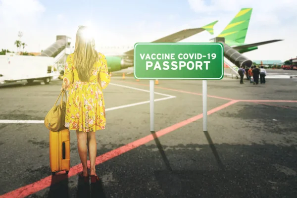 空港でワクチンCovid 19パスポートテキストで立っている間に荷物とハンドバッグを持っているブロンドの女性 — ストック写真