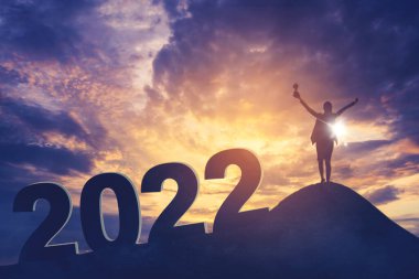 Mutlu iş kadınının silueti elinde bir kupa tutarken tepede başarısını 2021 numarayla kutluyor ve gündoğumu gökyüzü arka planıyla ayakta duruyor.