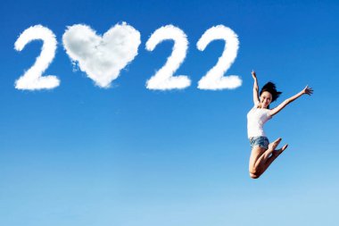 Bulutlarla atlayan neşeli kadın 2022 numara ve mavi gökyüzünde kalp sembolü.