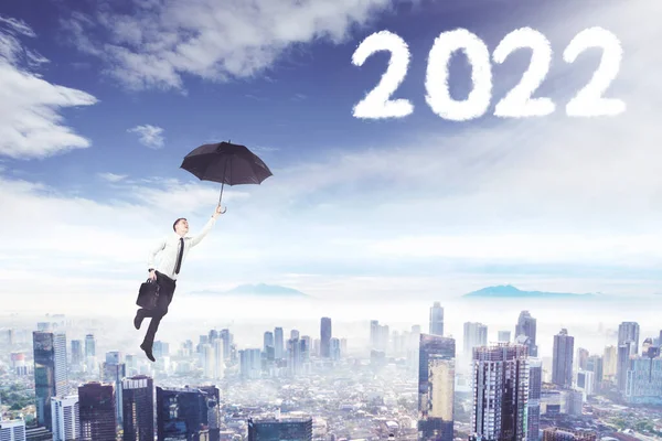 Young Businessman Using Umbrella While Flying Clouds Shaped Numbers 2022 — Stock Photo, Image