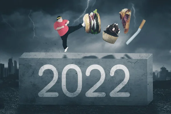 照片上的肥胖男子站在石头上 一边踢垃圾食品和香烟 一边站在乌云密布的天空背景下 2022年的数字 — 图库照片
