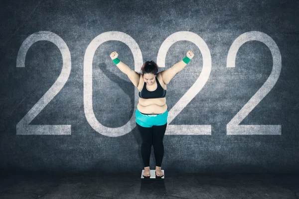 Obesity woman standing on the scale while expressing happy after success lose weight with 2022 number background