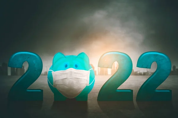 Close up of piggy bank wearing face mask with 2022 numbers in cloudy sky background