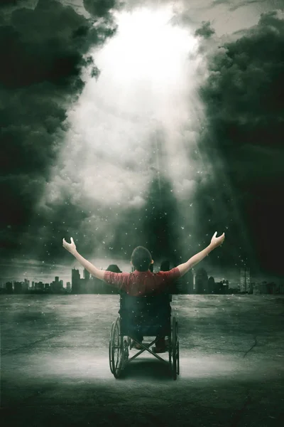 街並を背景に 空に明るい光の下で手を上げながら車椅子に座る障害者の後ろ姿 — ストック写真
