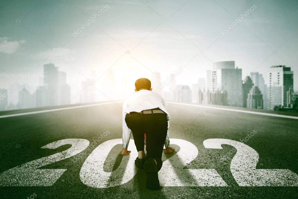 Rear view of young businessman ready to run toward a misty city while kneeling above 2022 numbers on on the road