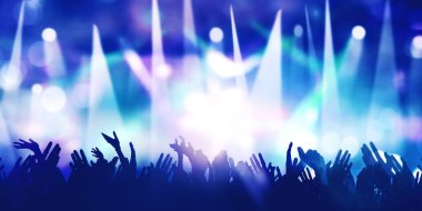 Kalabalığın silueti, insanların elleri, arka planda bulanık sahne ışıklarıyla müzik konserinin keyfini çıkarırken mutlu olduklarını gösteriyor.