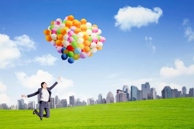 Şehir manzarası olan parkta dururken bir sürü balonla uçan mutlu iş kadını.