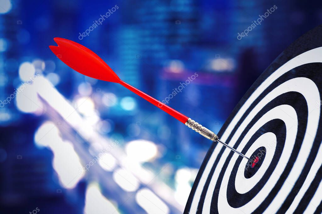 Close up of red dart on center of dartboard with blurred glowing night city background