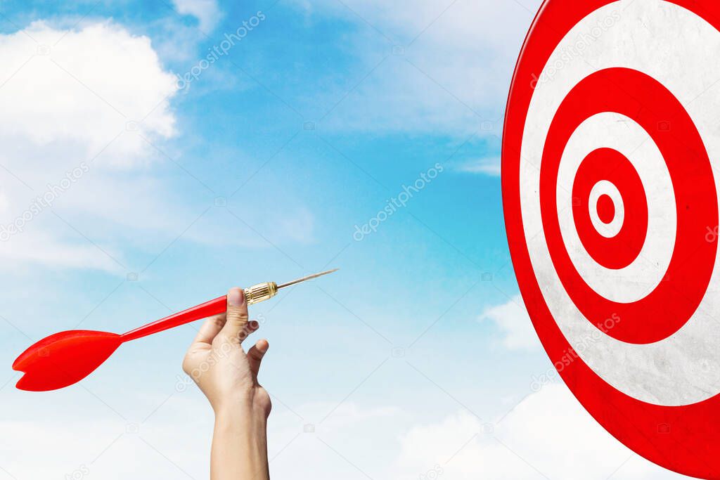 Business target concept. Close up of businessman hand throwing a red dart to target with blue sky background