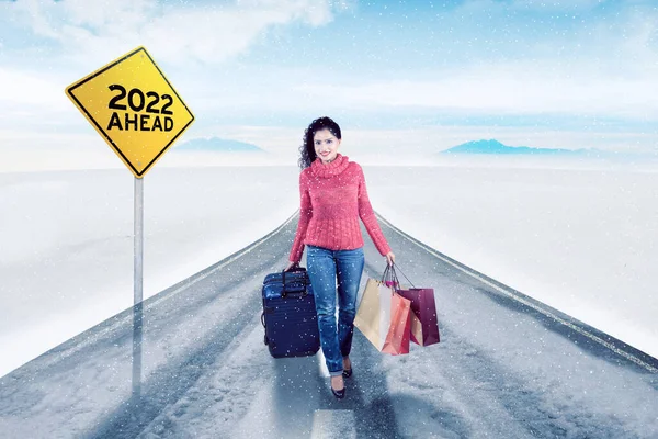 在冬季 年轻女子背着行李和购物袋 站在黄色路标上 前面印有2022年的字样 — 图库照片