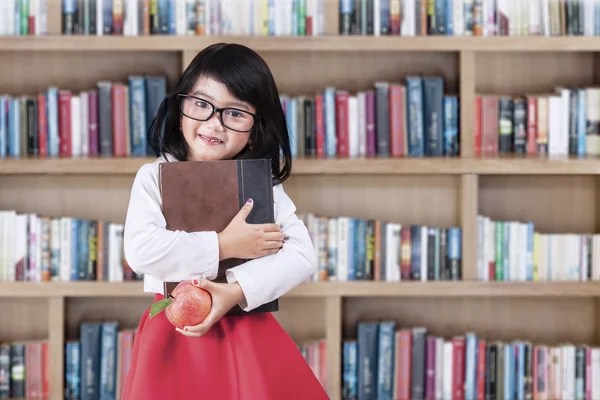 Colegiala con un libro y manzana en la biblioteca —  Fotos de Stock