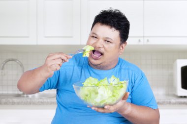 Adam mutfakta salata yiyor.