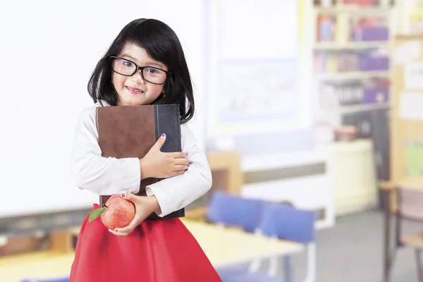 Школьная девочка держит книгу и яблоко в классе — стоковое фото