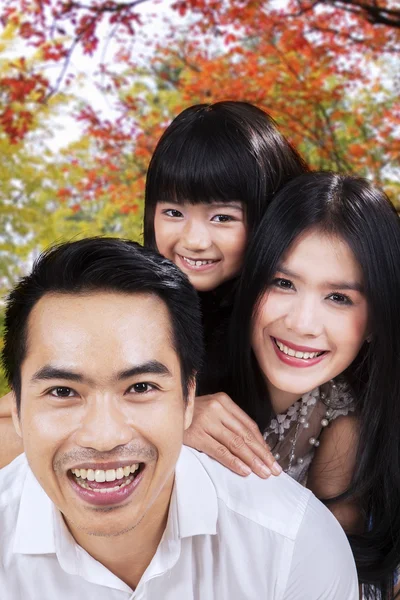 Atractiva familia sonriendo bajo el árbol de otoño —  Fotos de Stock