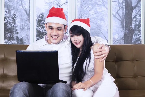 Casal com chapéu de Papai Noel e laptop no sofá — Fotografia de Stock