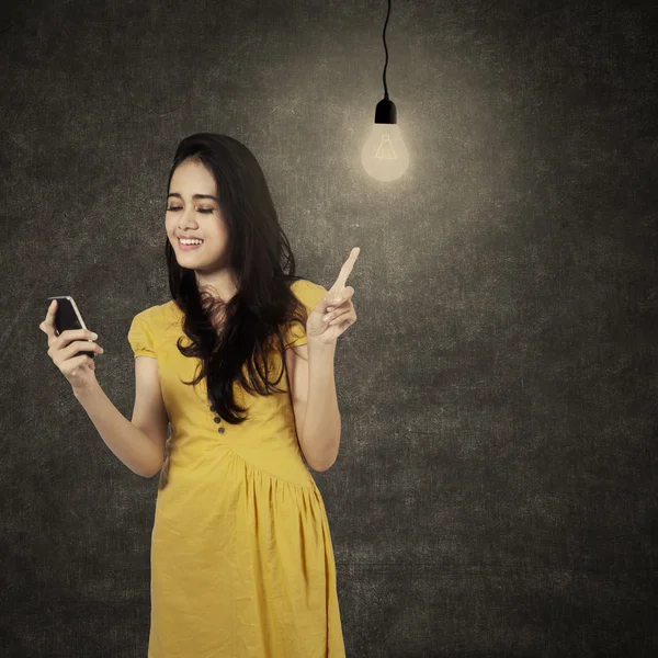 Jonge vrouw met cellphone onder gloeilamp — Stockfoto