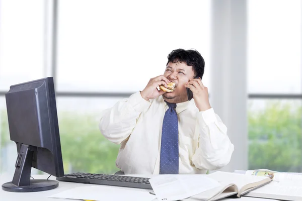 Hombre trabajador comiendo hamburguesa en la oficina — Foto de Stock