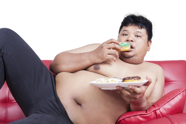 Ожирение человек ест пончики на диване — стоковое фото