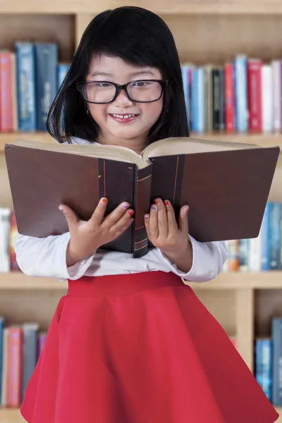 Menina bonita com livro na biblioteca — Fotografia de Stock