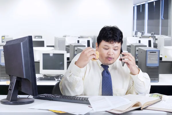 Empresário segurando hambúrguer enquanto trabalhava — Fotografia de Stock