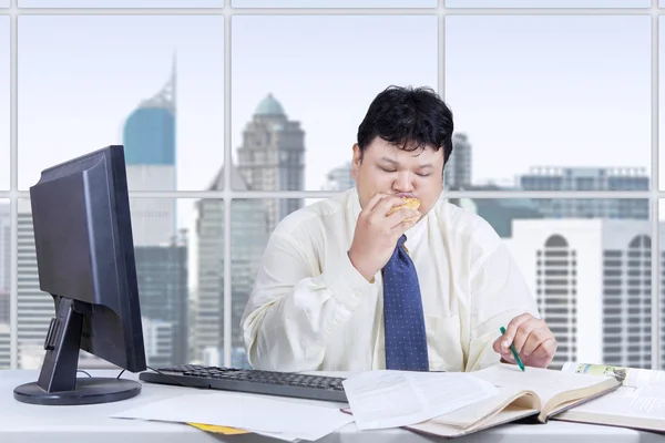 Gerente com fome trabalhando enquanto come hambúrguer — Fotografia de Stock