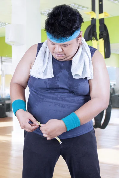 Человек с избыточным весом измеряет свой живот в спортзале — стоковое фото