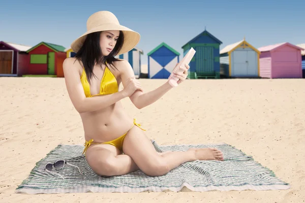 Ragazza che utilizza la protezione solare con sfondo spiaggia — Foto Stock