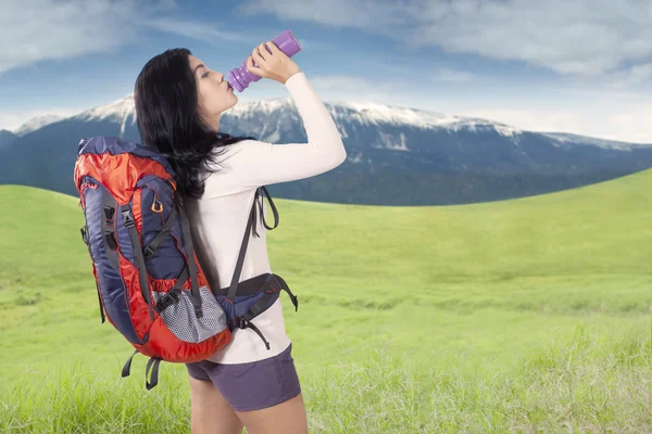 Woman with backpack drinks water at hill — Stock Photo, Image