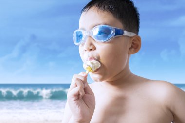 Male kid bites ice cream at seaside clipart