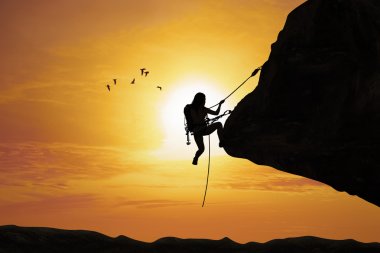 Silhouette of woman climbing on rock clipart