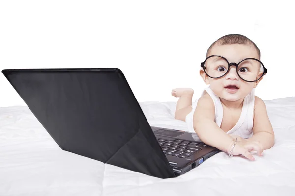 Söt baby med laptop och glasögon på sängen — Stockfoto