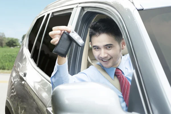 Homem dentro de um carro e mostrando uma chave de carro — Fotografia de Stock