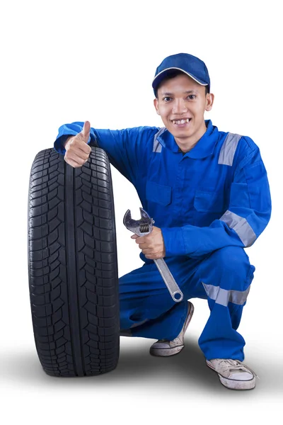 Mladý mechanik s pneu ukazuje palec — Stock fotografie