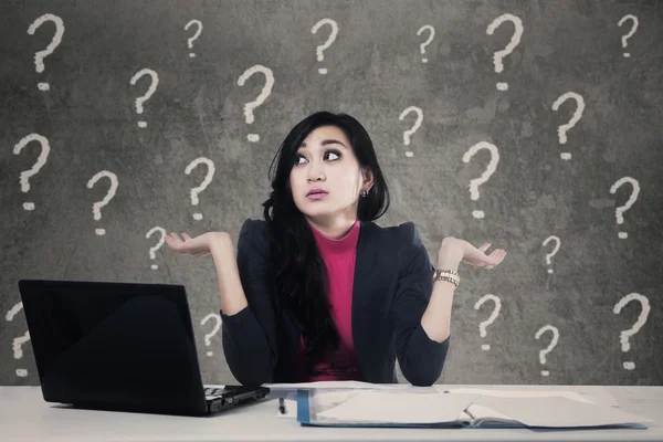 Verward vrouw met vraagtekens in office — Stockfoto