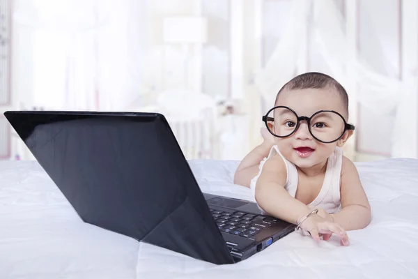 Söt baby med glasögon och laptop på sängen — Stockfoto