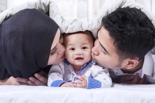 Muslim parents kiss their baby under blanket — Stock Photo, Image