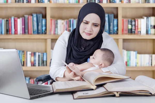 Mujer con bebé leyendo libros en la biblioteca — Foto de Stock