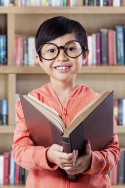 Cheerful little girl studying with book in library