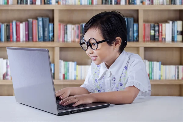 Hermosa niña escribiendo en el ordenador portátil en la biblioteca — Foto de Stock