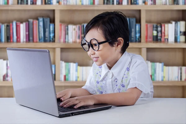 Lovely little girl typing on laptop in the library — 스톡 사진