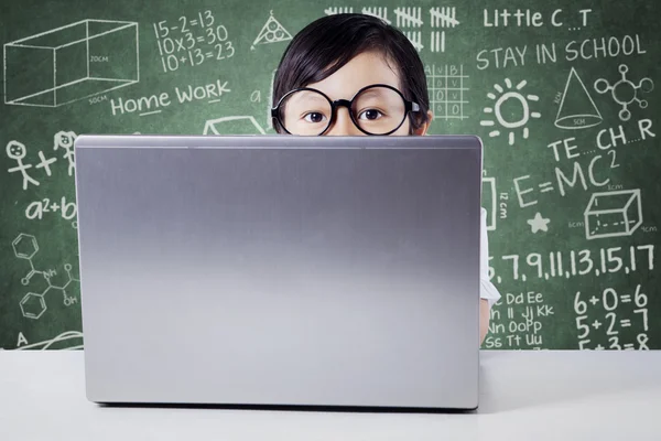 Girl with laptop peeking in the classroom — Stock Photo, Image