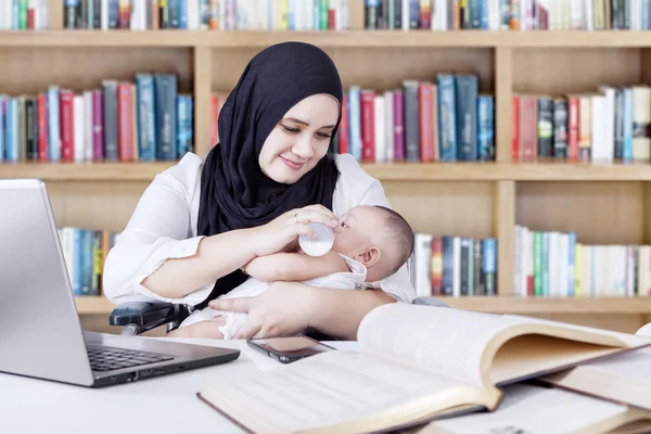 Hübsche Mutter arbeitet, während sie ihr Baby füttert — Stockfoto