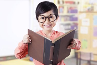Adorable kid holding textbook in classroom
