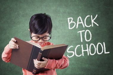Kid back to school and reading a book in class