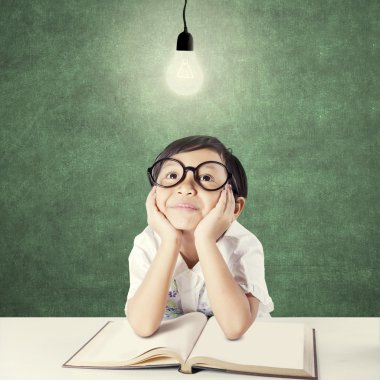 Pensive kid with textbook sitting under lightbulb