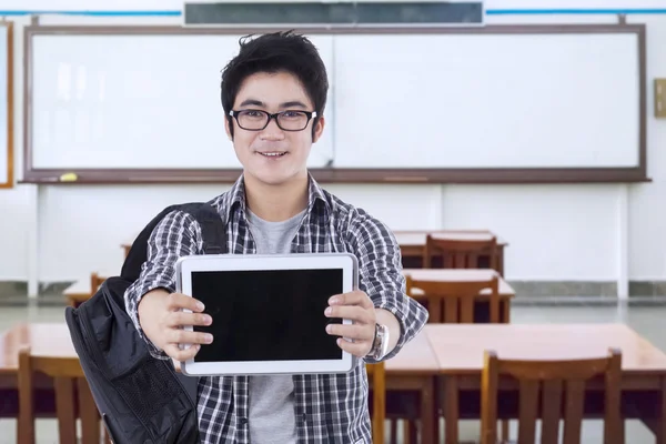 Estudante do sexo masculino em pé na sala de aula e mostra tablet — Fotografia de Stock