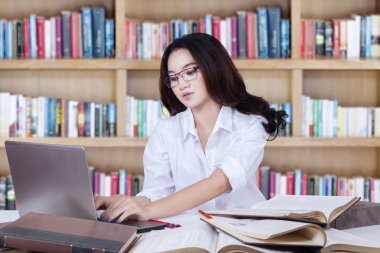 Cute student typing on laptop in library