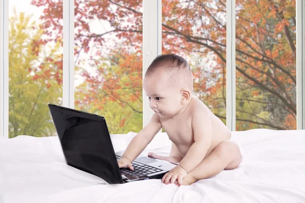 Curious baby with laptop on bed — Stockfoto