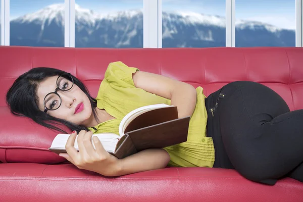 Pretty woman lying on sofa while reading book — Stok fotoğraf